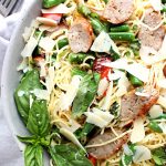 A bowl of grilled Italian sausage pasta with garden beans, fresh basil, red peppers, and a lemon dressing.