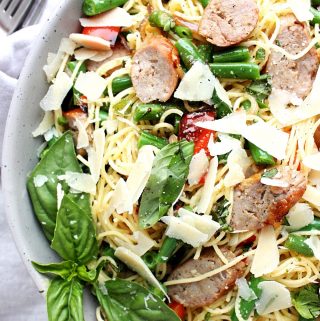 A bowl of grilled Italian sausage pasta with garden beans, fresh basil, red peppers, and a lemon dressing.