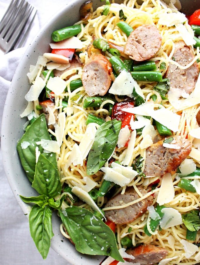 A bowl of grilled Italian sausage pasta with garden beans, fresh basil, red peppers, and a lemon dressing.