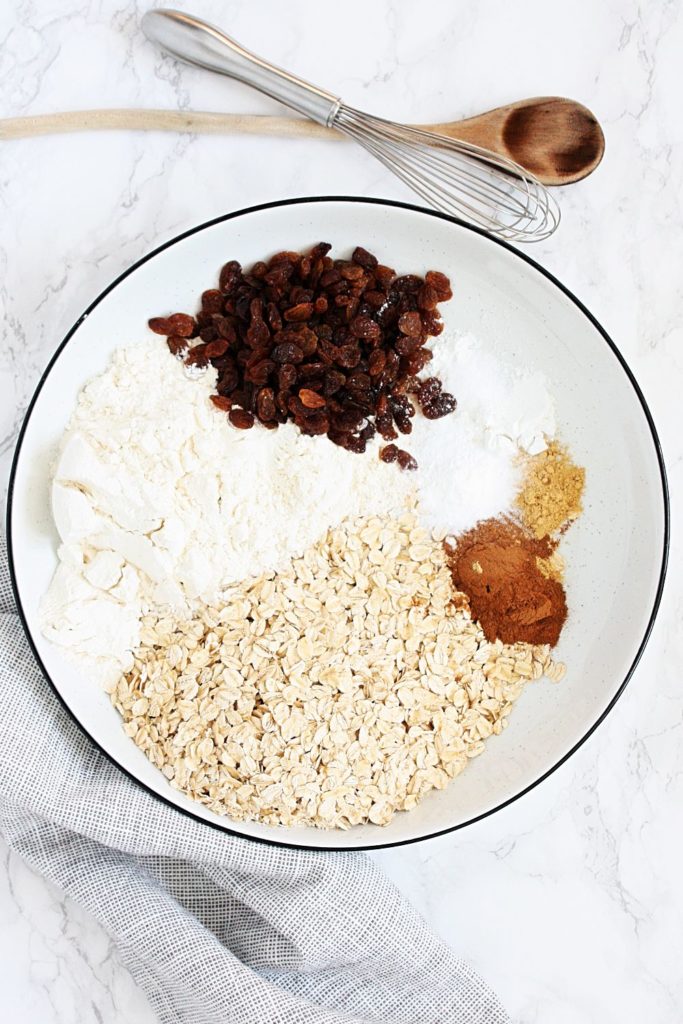 Mixing bowl with dry ingredients: oats, flour, raisins, cinnamon, ginger, baking soda and baking powder.