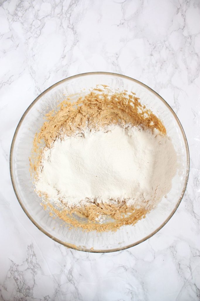Adding flour to the peanut butter cookie batter in a mixing bowl.