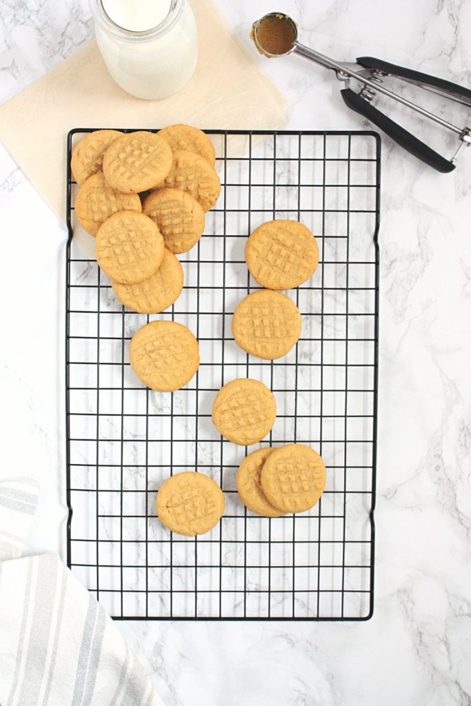 Peanut Butter Shortbread Cookies on a baking rack with a bottle of milk and a cookie scoop