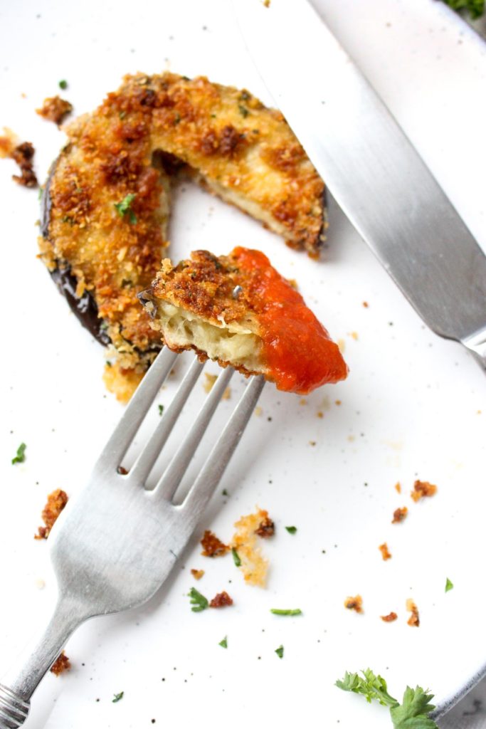 A bit of crispy eggplant dipped in marinara on a fork.