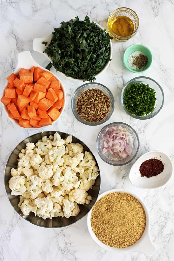 Couscous salad ingredients: whole wheat couscous, chopped sweet potatoes, cauliflower florets, chopped kale, sliced shallots, chopped chives, sunflower seeds, olive oil, salt and pepper, and sumac.